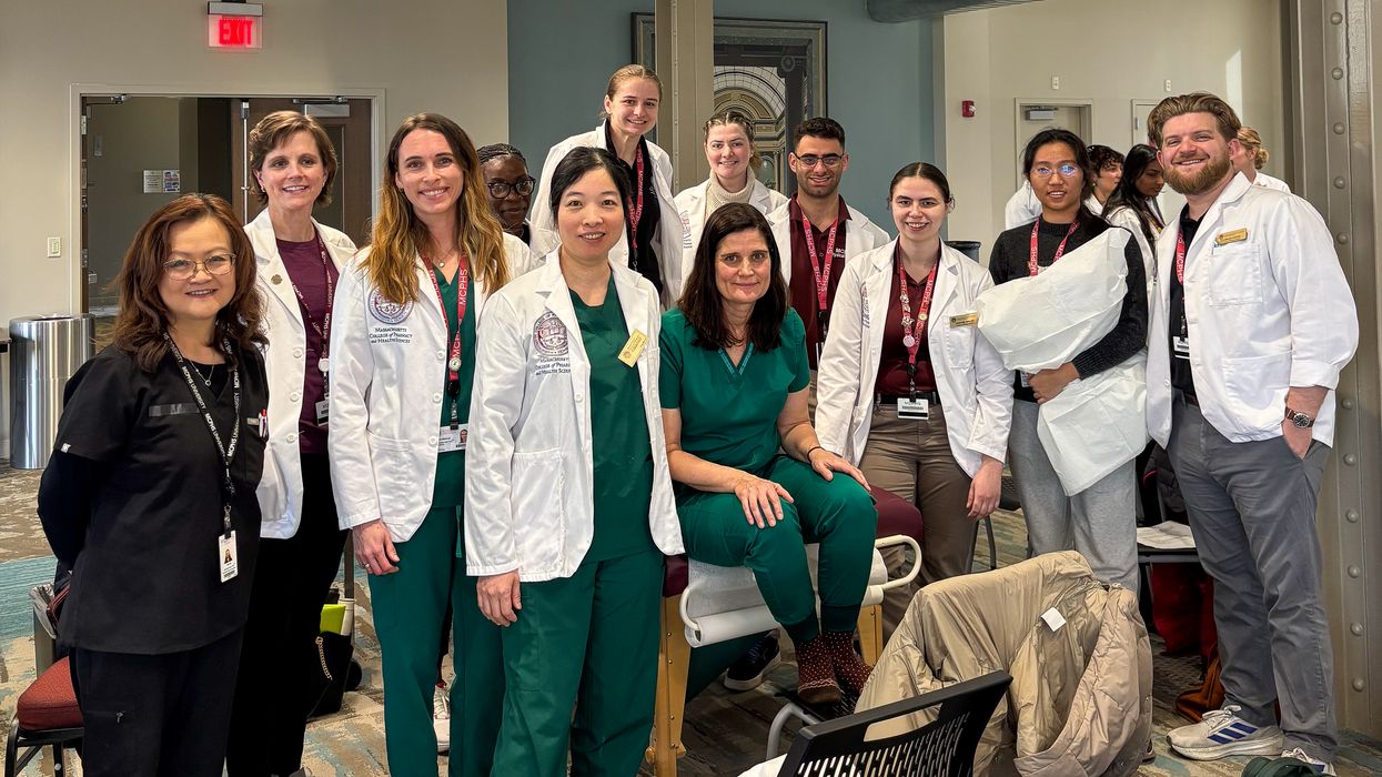 A group of students from MCPHS, most wearing white coats, stand next to each other and smile for a photo.