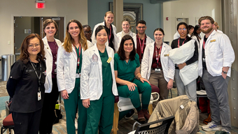 A group of students from MCPHS, most wearing white coats, stand next to each other and smile for a photo.