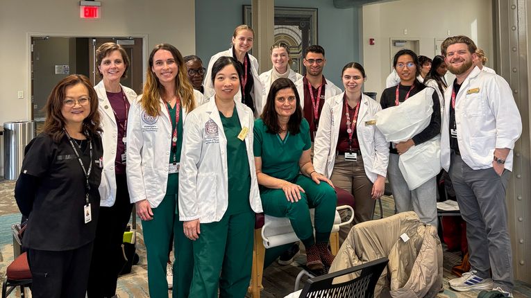 A group of students from MCPHS, most wearing white coats, stand next to each other and smile for a photo.