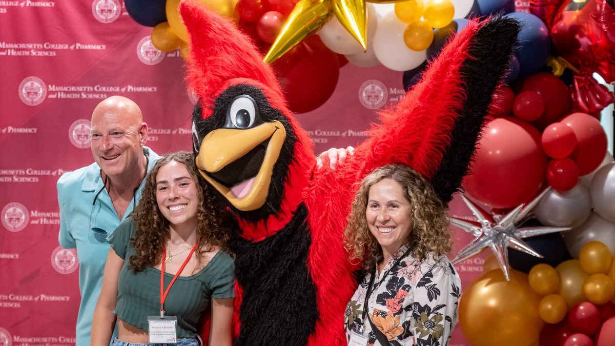 Parents and student stand with the MCPHS mascot, Red.