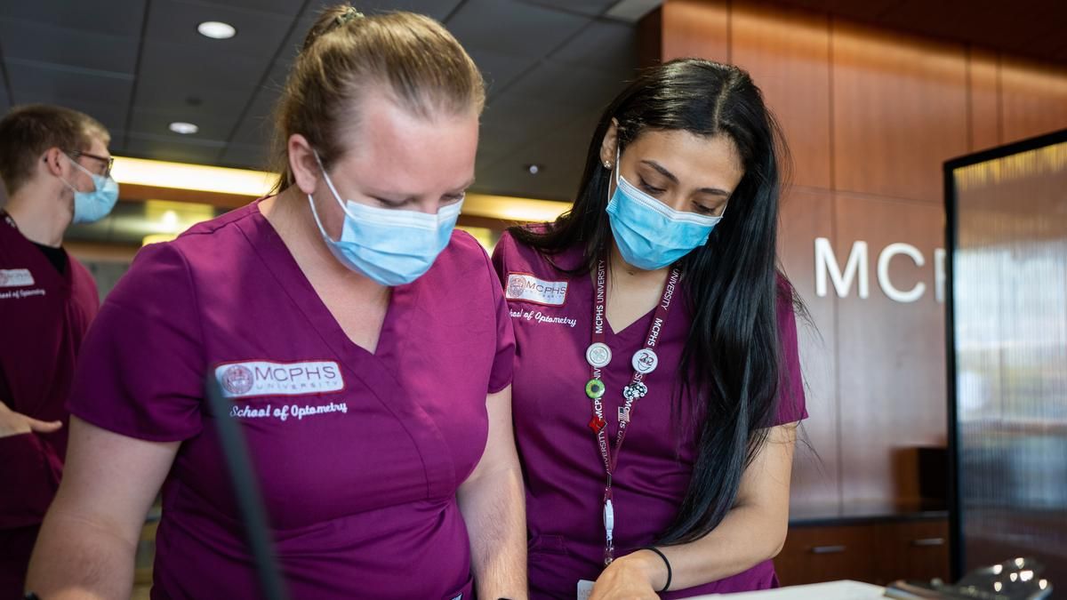 Two female students wearing scrubs and lanyards. 