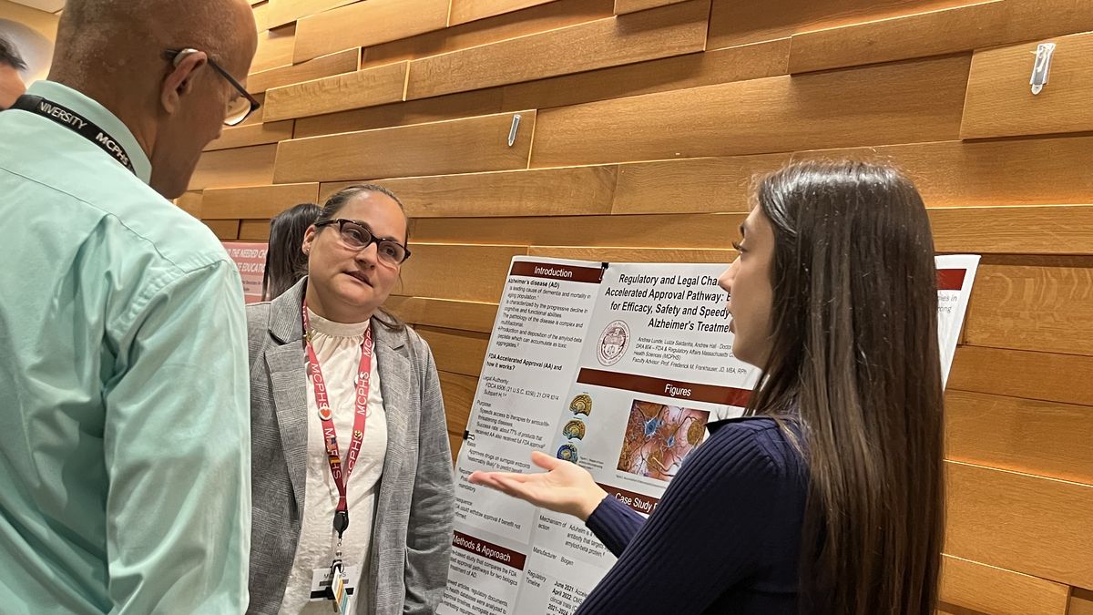 Two women and a man discuss a poster.