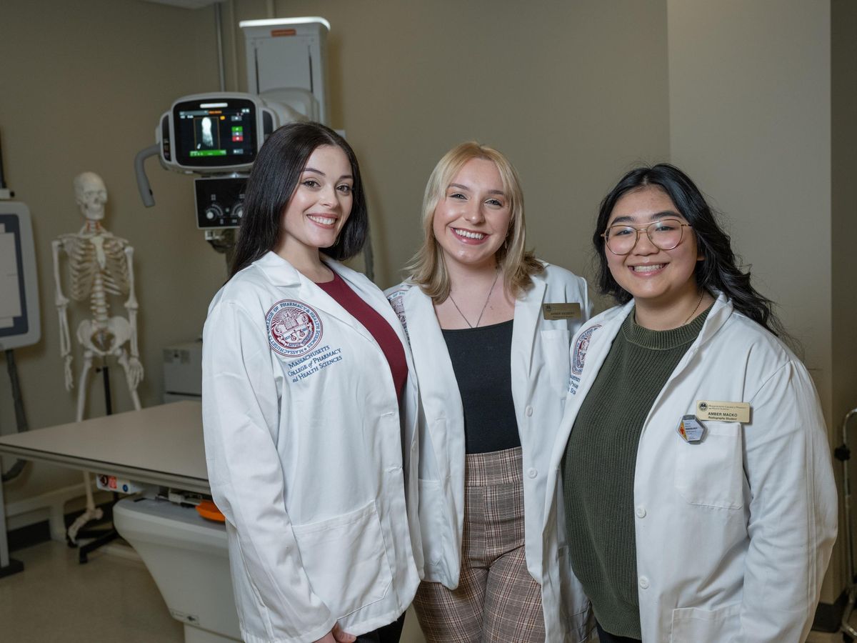 Three students wearing white coats and smiling. 