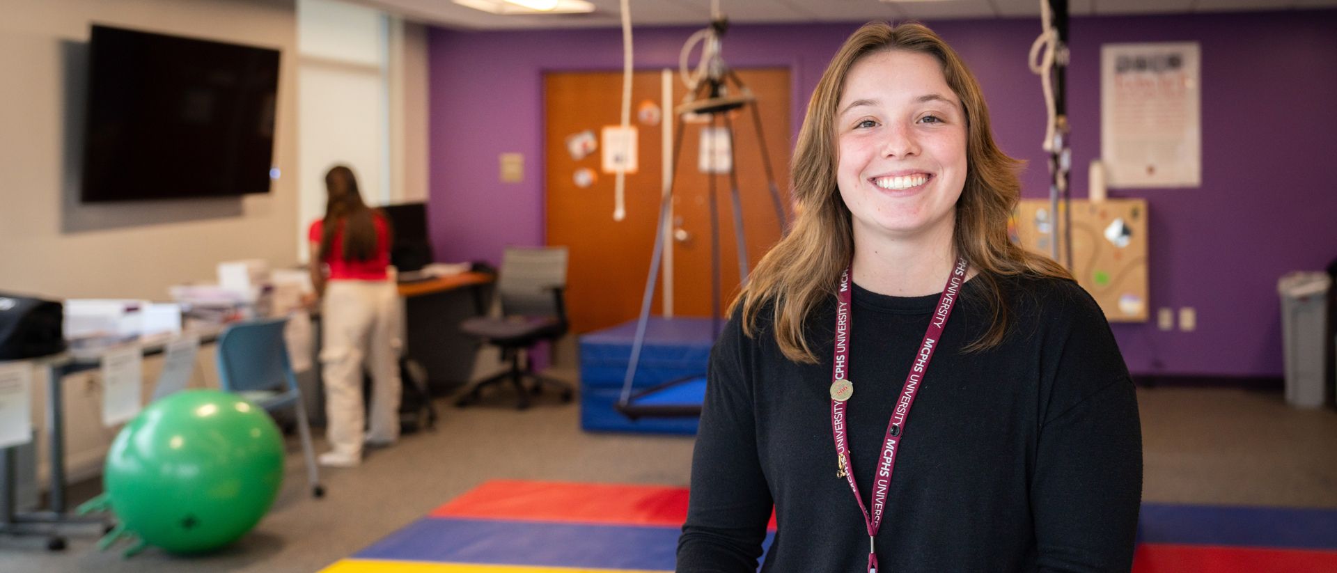 Smiling Occupational Therapy student wearing an MCPHS lanyard. 