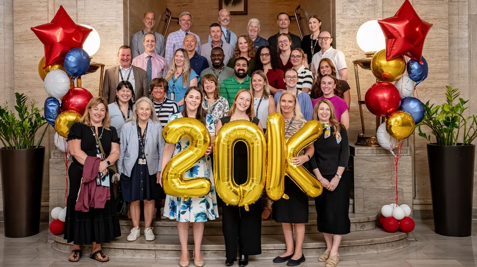 Members of the MCPHS School of Professional Studies team stand on stairs with 20K balloons.