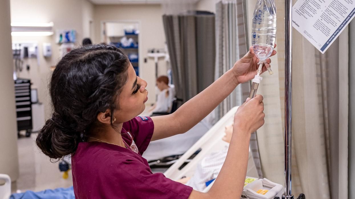MCPHS female nursing student checking an IV bag. 