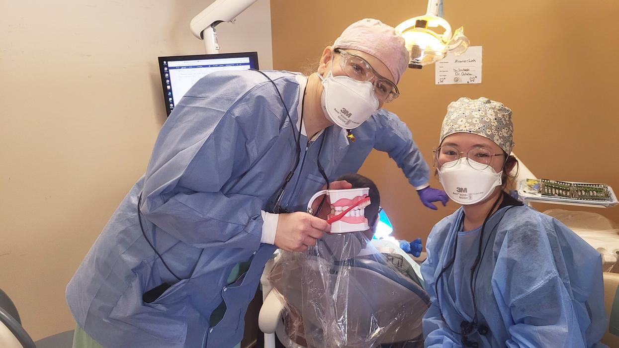 A professor and student-hygienist smile under their masks as they hold up a toothbrush and dental model.