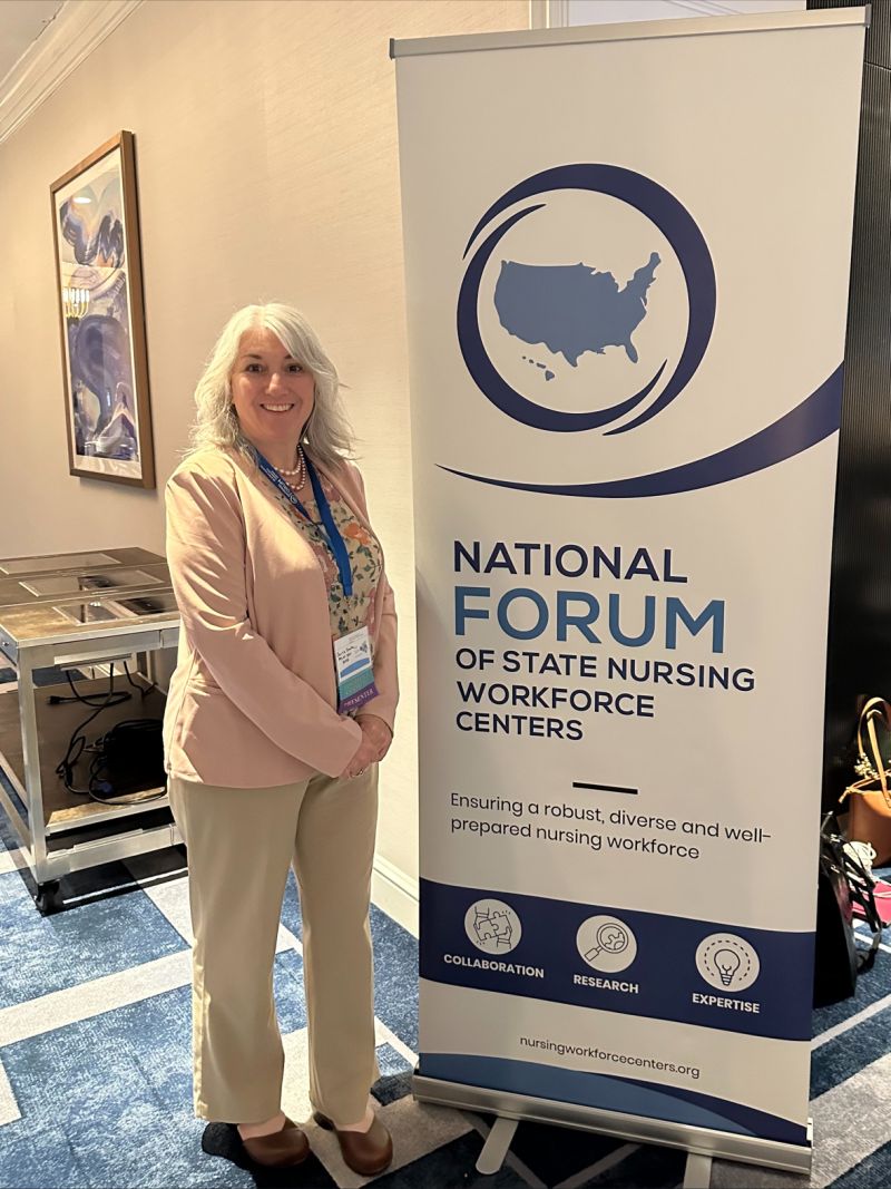 Assistant Professor Carla Smith stands in front of a nursing conference sign.