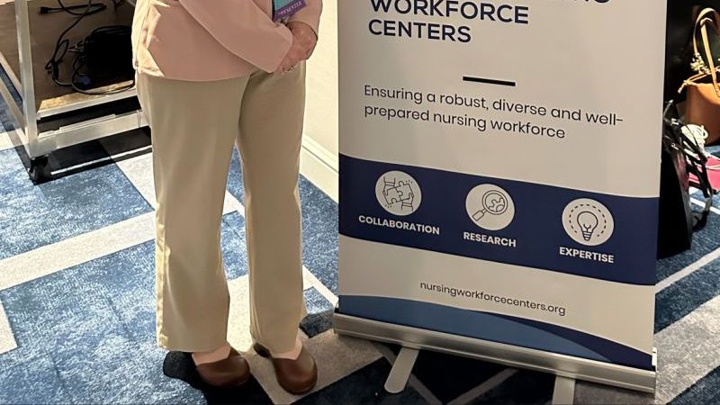Assistant Professor Carla Smith stands in front of a nursing conference sign.