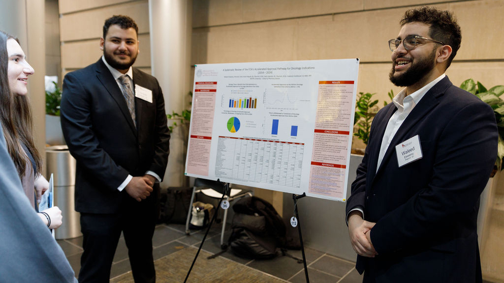 People stand in front of a poster at the MCPHS Boston Student Research Conference
