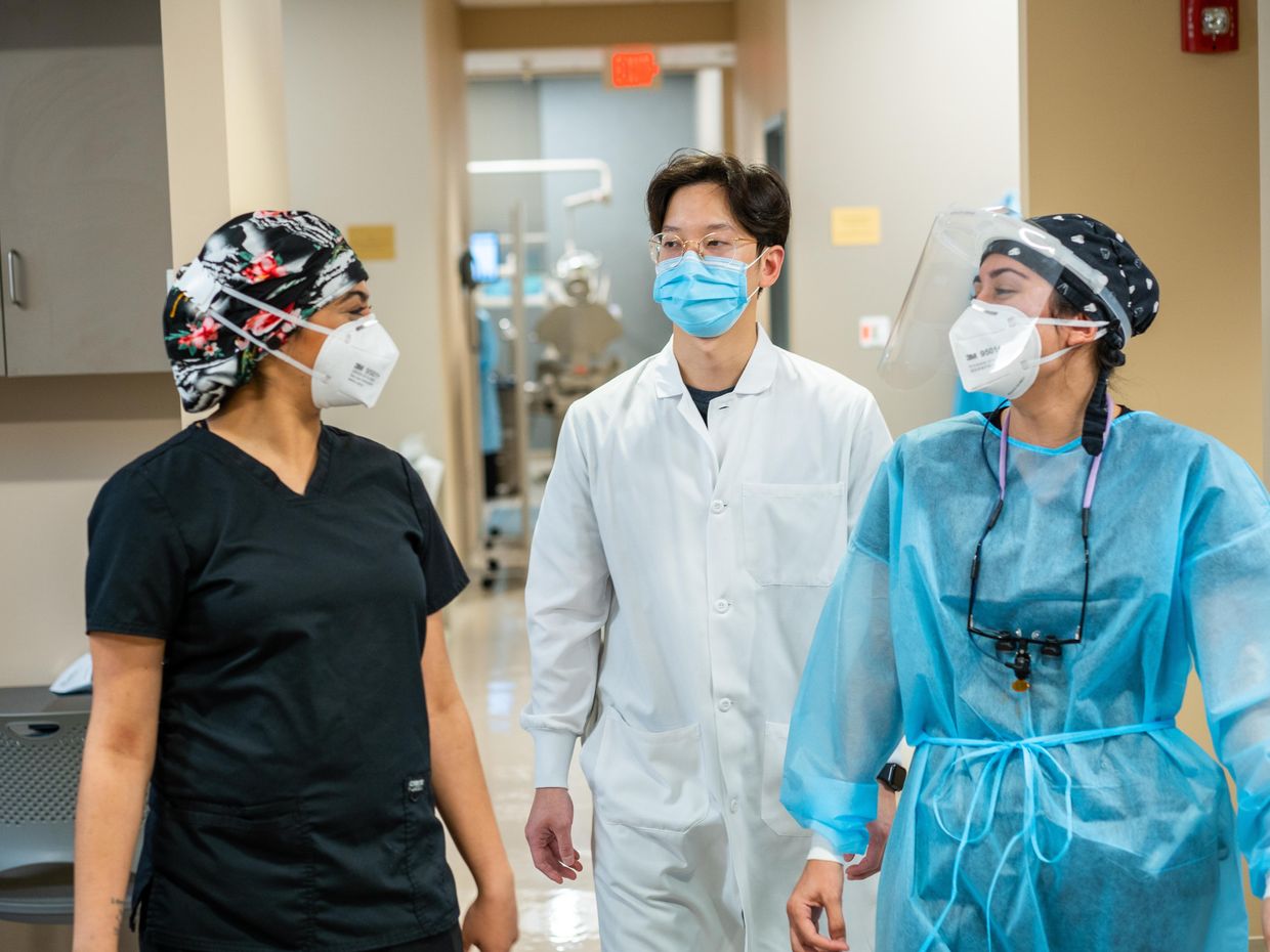 Three students wearing masks walking down a hallway. 