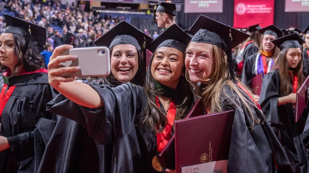 Three students wearing graduation robes taking a selfie.