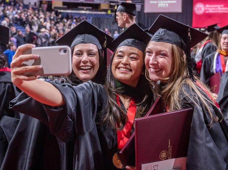 Three students wearing graduation robes taking a selfie.