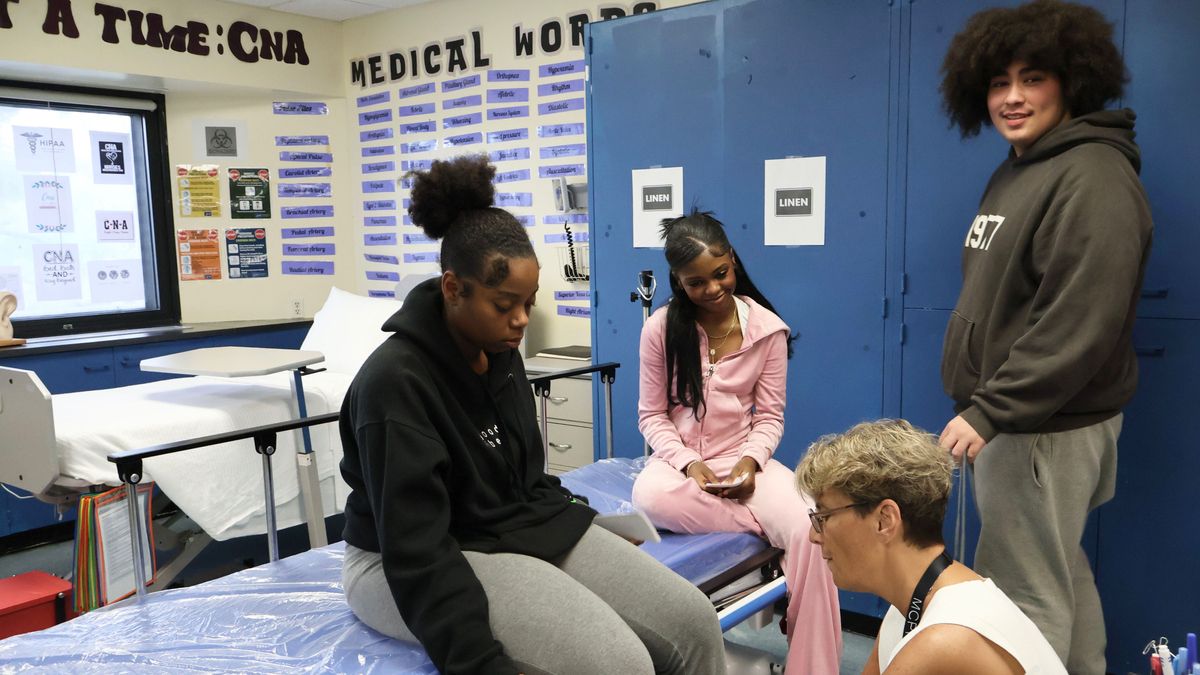 A woman exams a patient's knee while two other people watch.