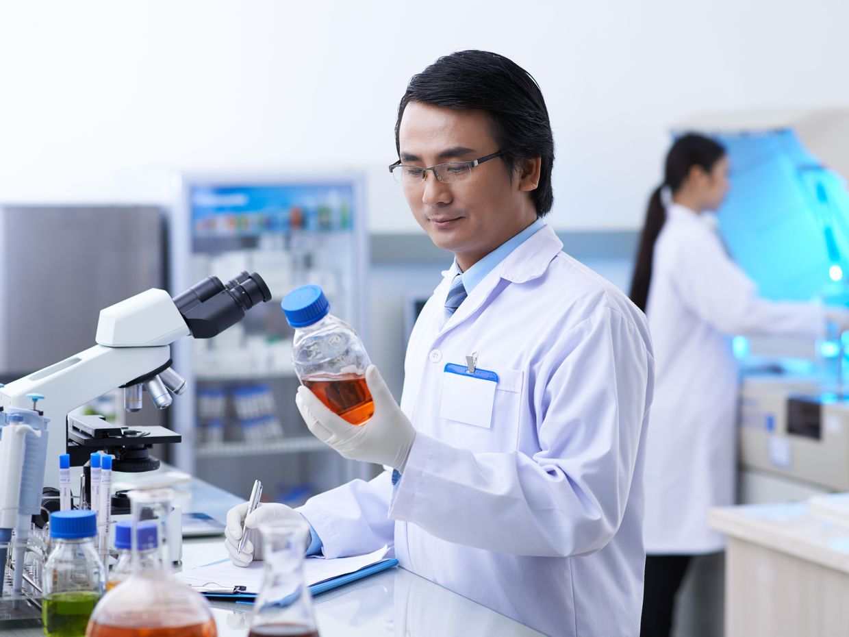 Male scientist in lab reading information on a bottle. 