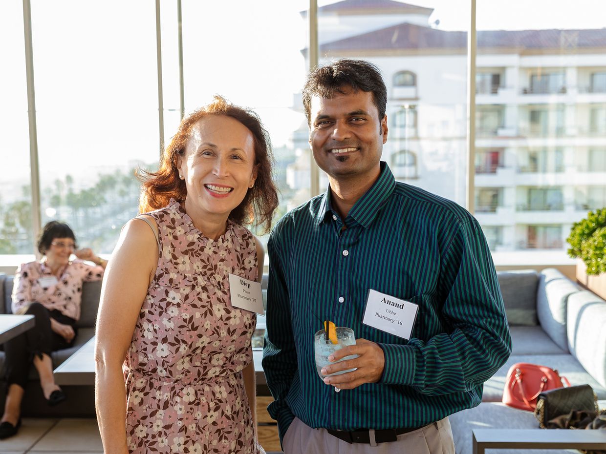 A man and a woman wearing MCPHS alumni name tags stand together at an indoor California alumni event.