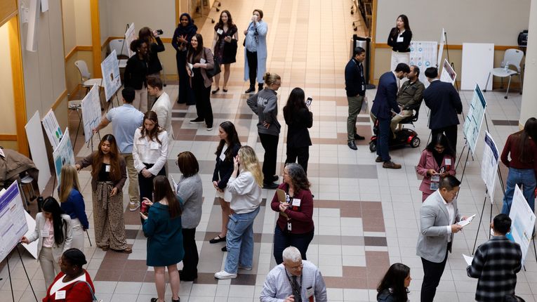 People stand in atrium looking at research posters.