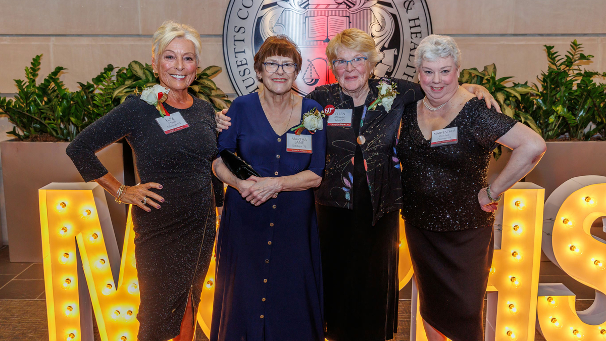 Four women stand in front of MCPHS letters at the Golden Graduates reunion.