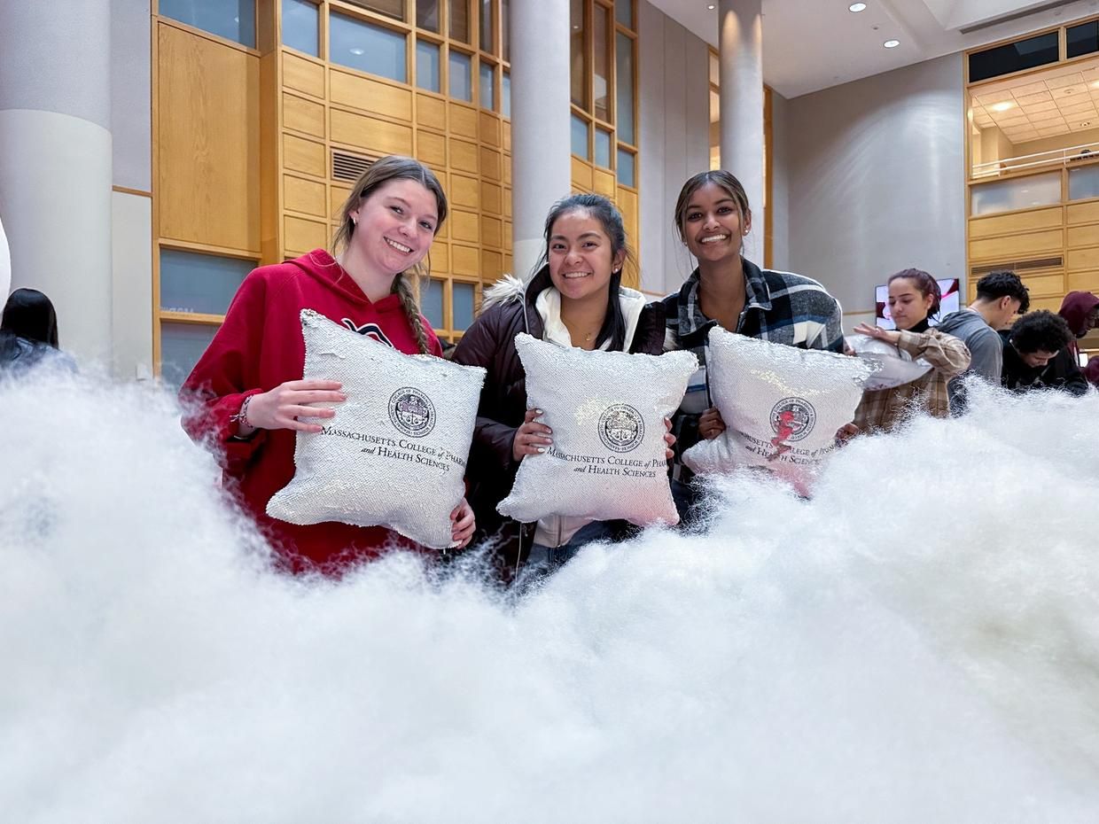 Three MCPHS students holding branded pillows they stuffed during a Campus Life event