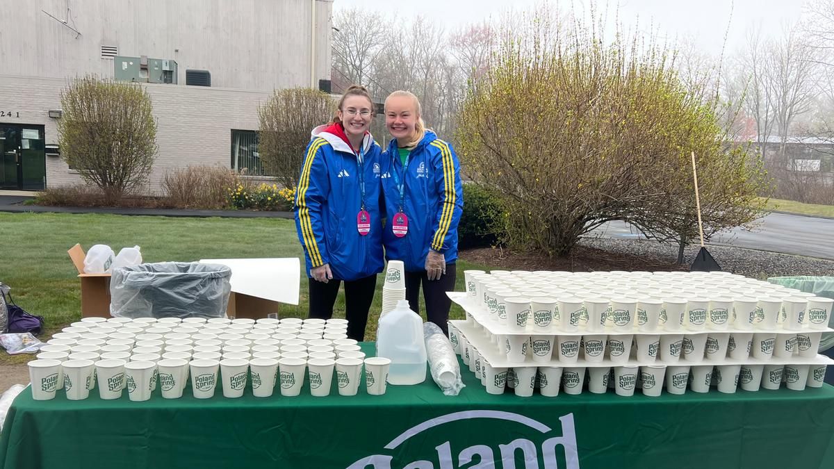 Two women standing in front of cups at the Boston Marathon.