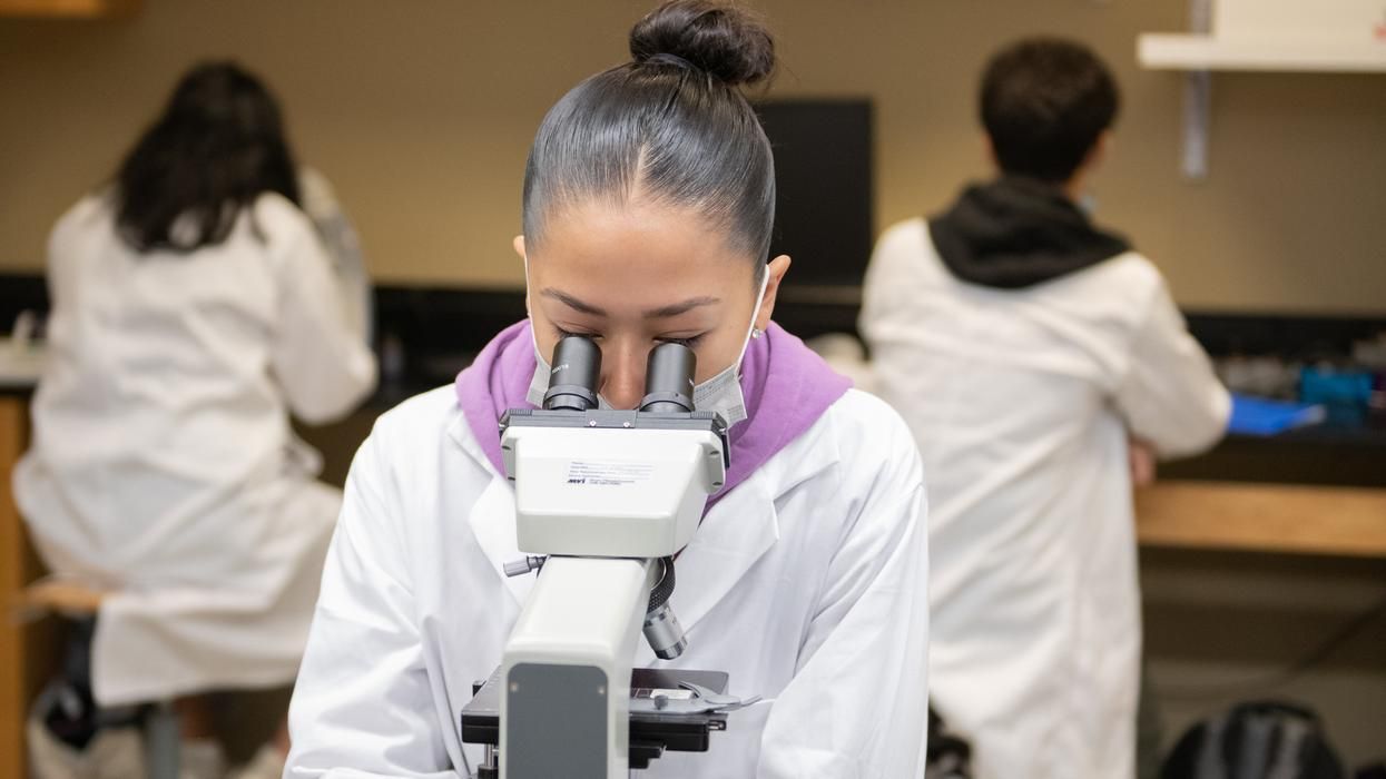 MCPHS student in the chemistry lab looking through a microscope. 