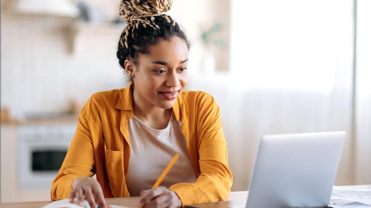 Woman looking at her computer and taking notes in a notebook. 