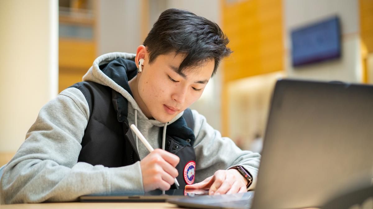 Male student sitting in front of laptop writing. 