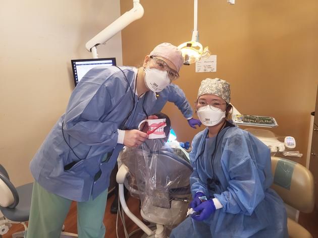 A professor and student-hygienist smile under their masks as they hold up a toothbrush and dental model.