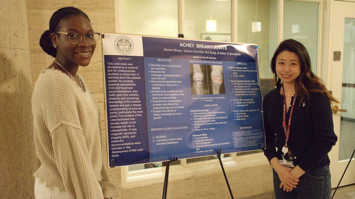 Two female students smiling in front of a poster. 
