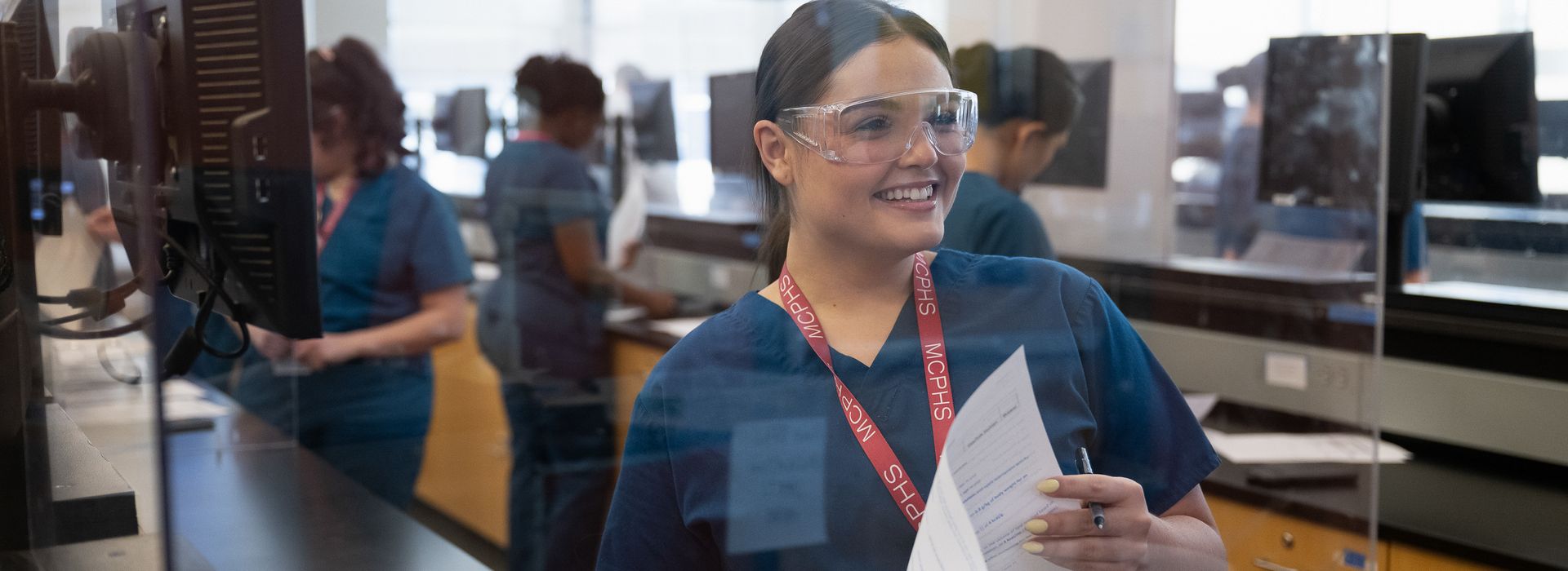 Female pharmacy student wearing scrubs in a lab environment. 