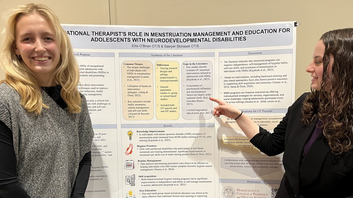 Two women stand in front of a poster.