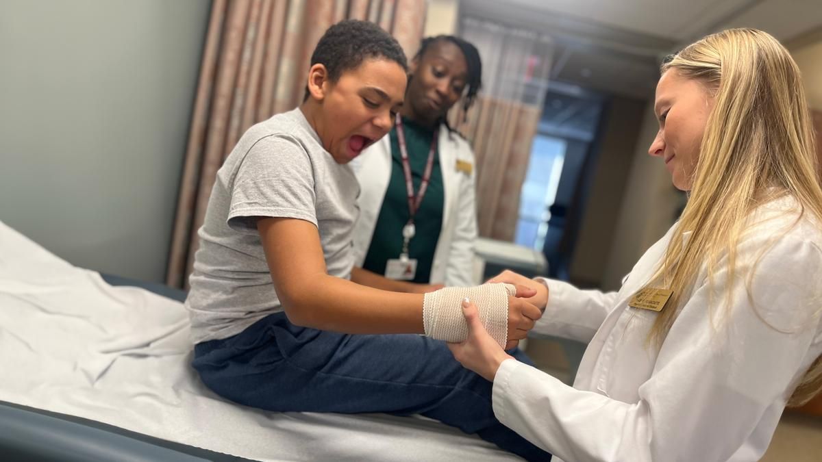 A sixth-grader from the Jacob Hiatt Magnet School gets his hand wrapped by a PA student during a recent field trip to MCPHS in Worcester.