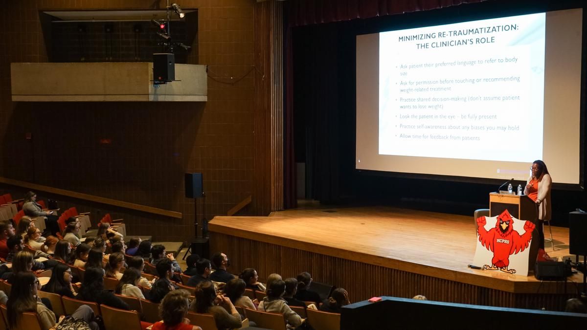 Chioma Tomlinson, PA-C, speaks on stage to an audience of PA students from MCPHS