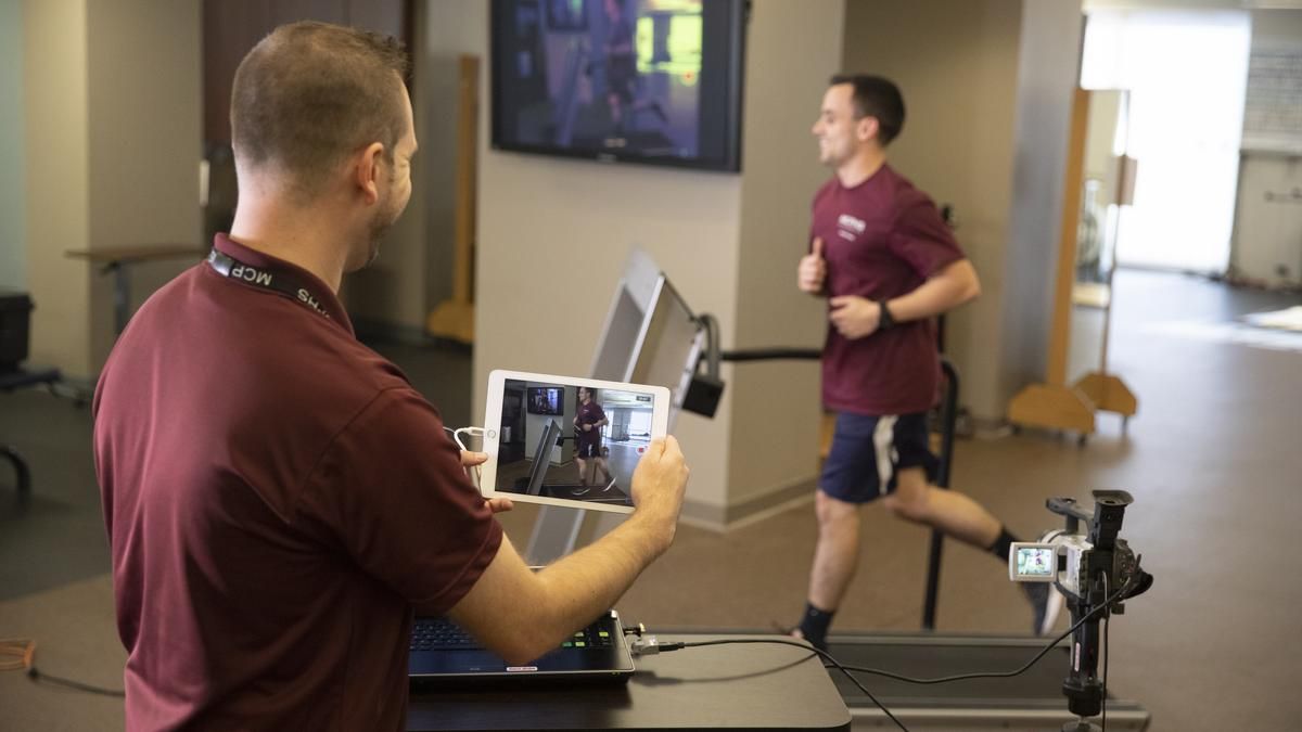 Physical therapy student using  computer and video equipment, watching another student run on the treadmill. 