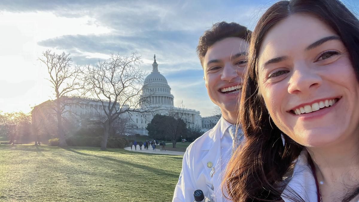 Two pharmacy students wearing white coats pose for a selfie outside the United States Capitol.