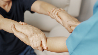 A healthcare provider holds the wrists of another person to help them stand up.
