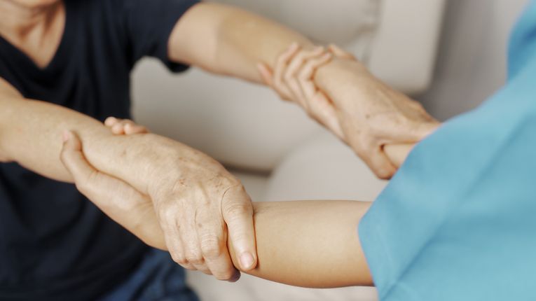 A healthcare provider holds the wrists of another person to help them stand up.