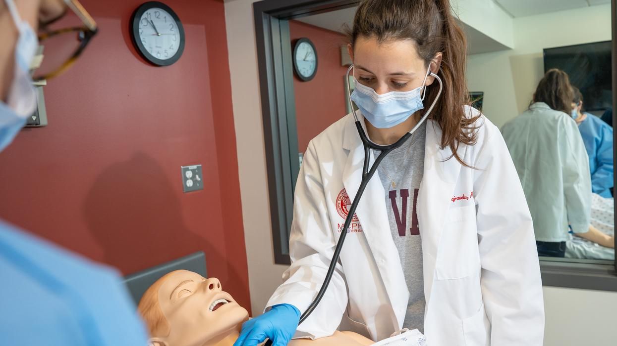 MCPHS Physician Assistant student wearing a stethoscope and placing it on a mannikin. 