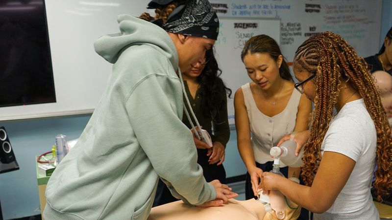 Angel Santana practices performing chest compressions on a CPR dummy.
