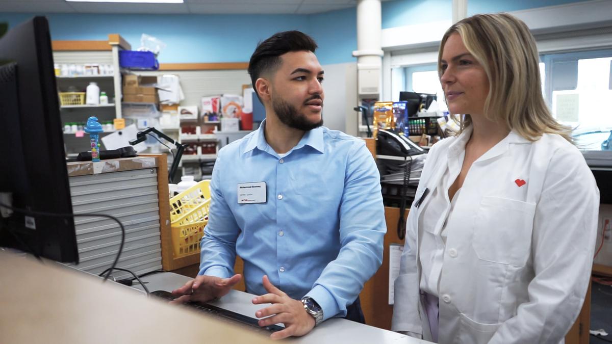 Muhammad Elsweesy standing at computer with woman in a pharmacy.