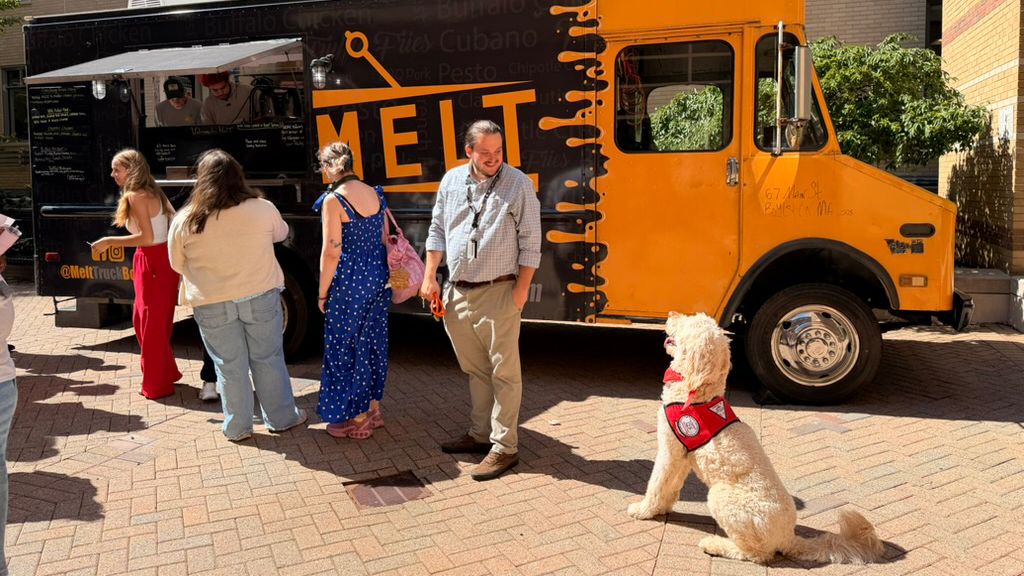 MCPHS's therapy dog, Woodman, sits in front of a food truck.