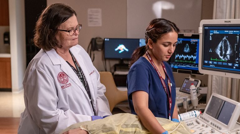 faculty member in white coat with student in scrubs in front of an MRI screen..jpg