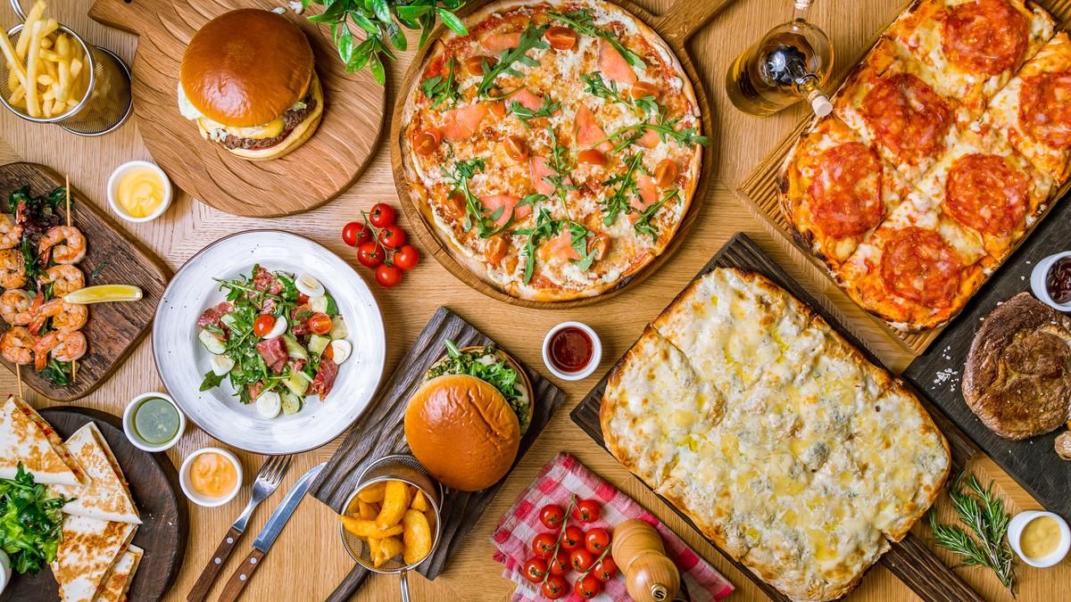 An array of traditional American dinner food, including pizza, a hamburger, shrimp, french fries, and vegetables on a table