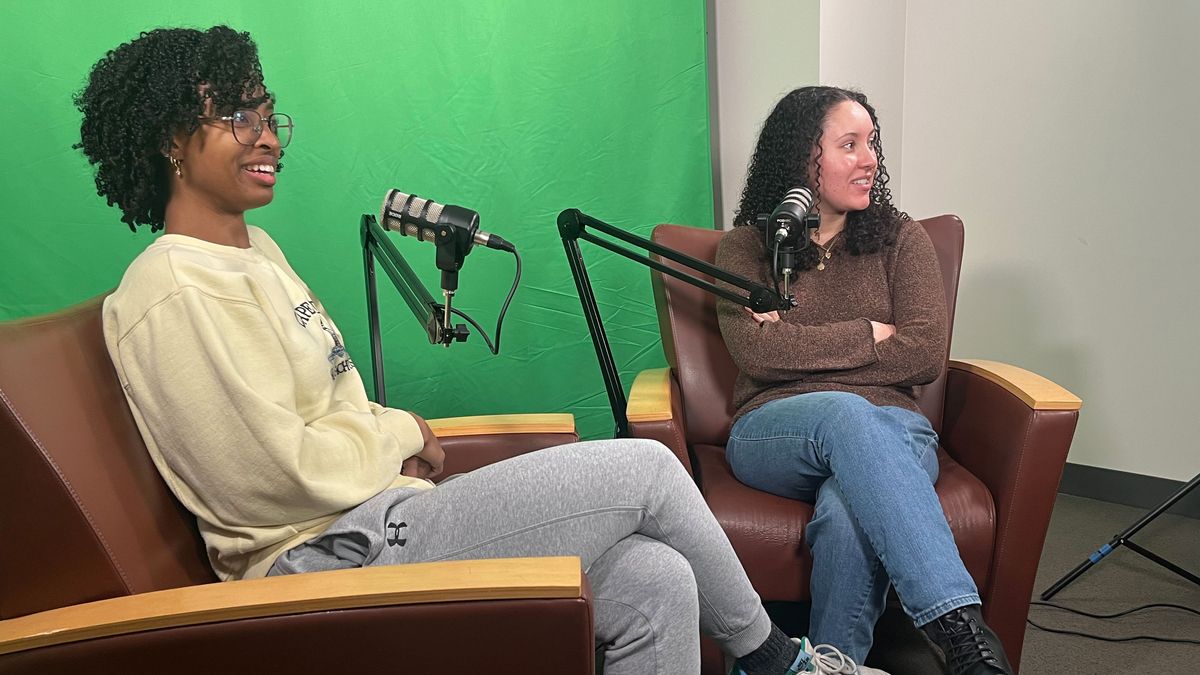 Emily Obuseh and Kyleigh Hill sit in front of microphones.