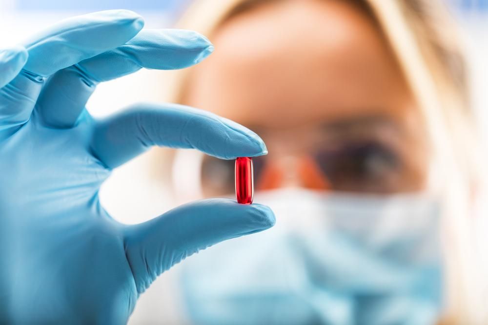 Close-up of a pill being held in a gloved hand by female scientist. 