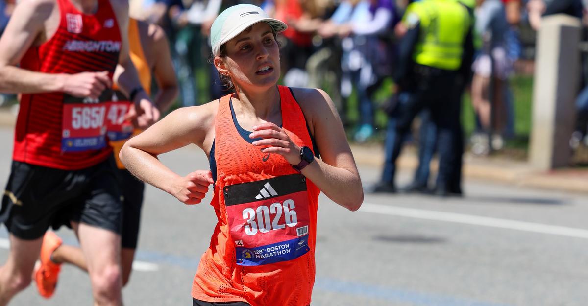 Arianna Maida, wearing bright orange tank top and white hat, pumps her arms while running during the Boston Marathon.