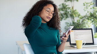 Woman holds neck while looking at phone.