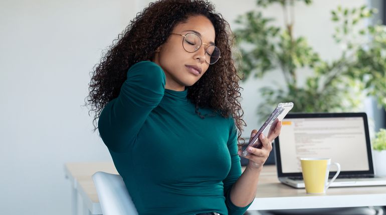 Woman holds neck while looking at phone.