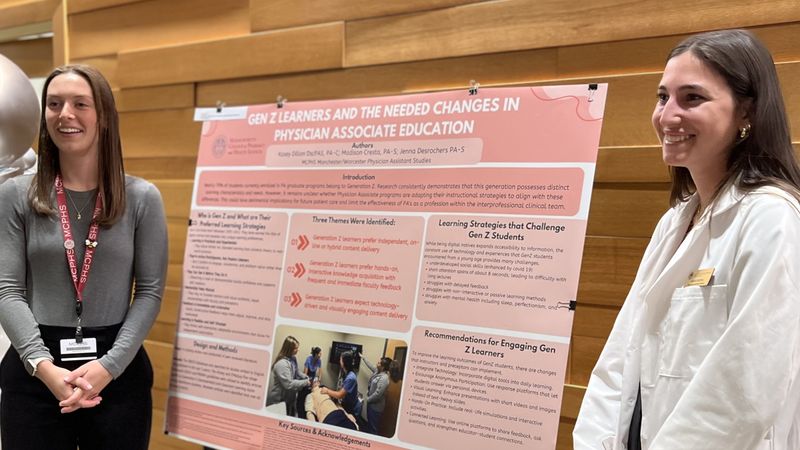 Two women stand in front of a poster.