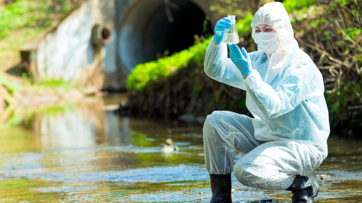 Environmental scientist in protective gear taking a water sample from sewage water.